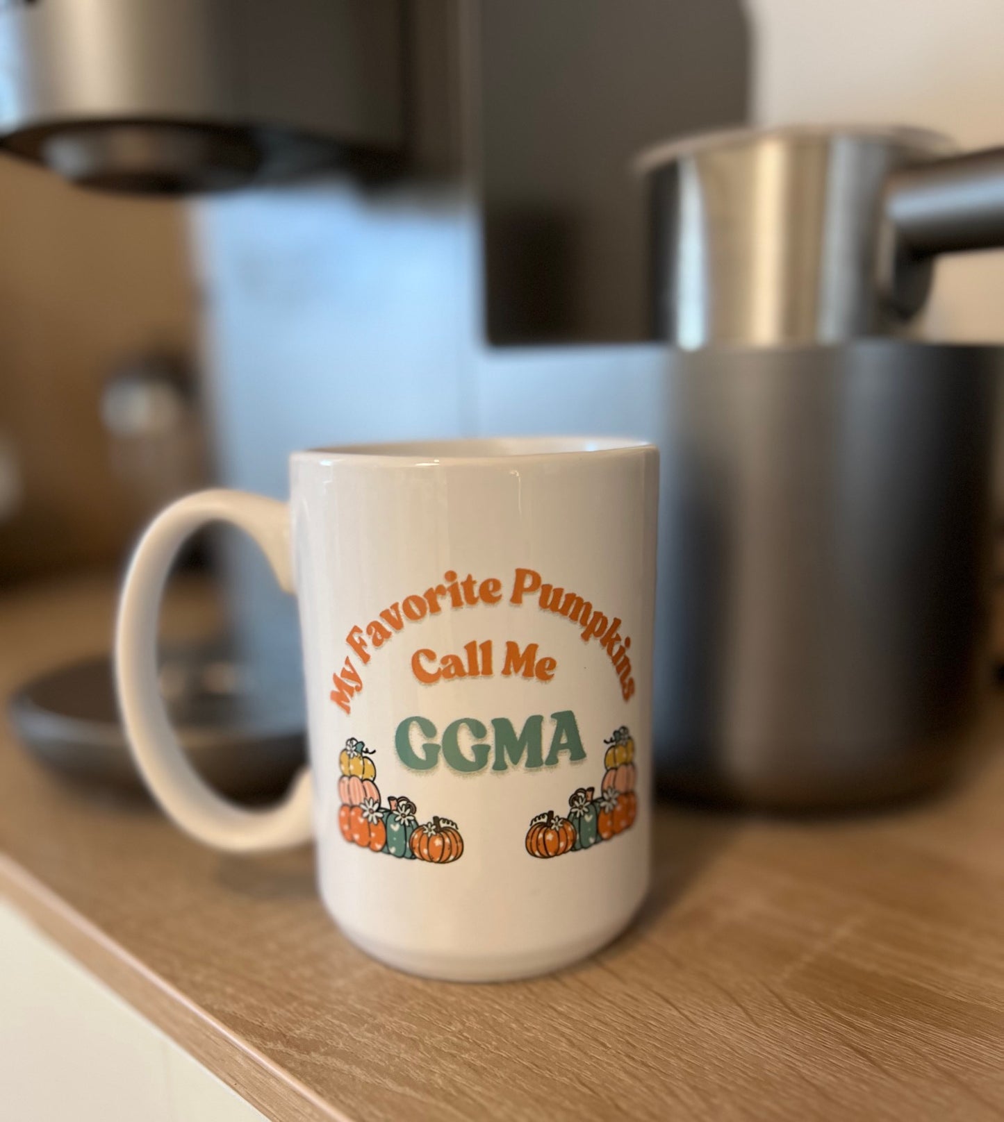 White mug with 'My Favorite Pumpkins Call Me GGMA' text and pumpkins design on a kitchen counter.